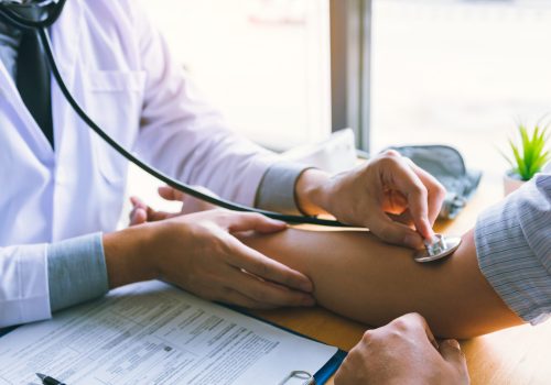 Asian doctor is using the stethoscope to touch the patient's arm.
