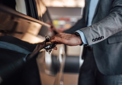 A male in a suit opens the door of his new car.