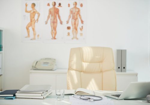 Desk of chief physician with laptop, planner, printed cardiograms and folders with medical histories of patients