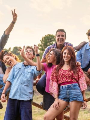 Joyful multigenerational group of friends and family celebrating outdoors. Diverse people of various ages and ethnicities enjoying time together in nature, sitting on a wooden fence - unity, happiness