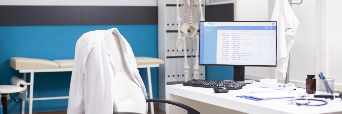 Empty medical office with no people inside, having clinical equipment and computer ready for healthcare use. Modern desktop pc in vacant hospital room displaying patient diagnostic data.