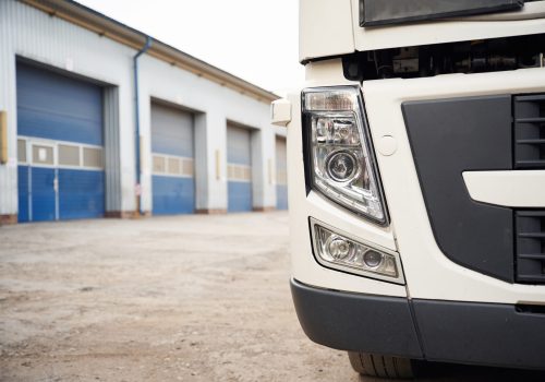 Front particle view of truck that is parked outdoors near garage.